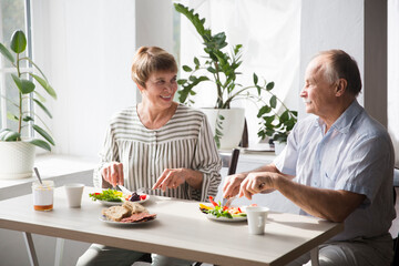 Portrait of relaxed fun senior couple together and eating breakfast in their kitchen at home
