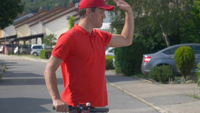 CLOSE UP: Reckless Caucasian courier drops two packages while riding an electric scooter. Postal service guy rides an e-scooter while unsuccessfully delivering parcels. Bad door to door shipping.