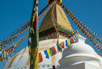 The upper part of the Boudhanath stupa in Kathmandu, Nepal. The image of Buddhas eyes on a gold surface of the stupa. Colorful prayer flags nearby.