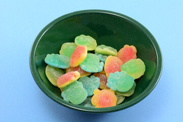 Juice filled gummy candies shaped into ocean creatures in green bowl on blue background