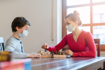 Fototapeta premium Mother and son playing chess to kill some time during curfew in crises
