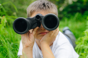 child boy in white t-shirt looking through binoculars in nature green landscape. Explore and discover wildlife concepts. kid adventure, searching for direction. imagination, freedom. copy space.
