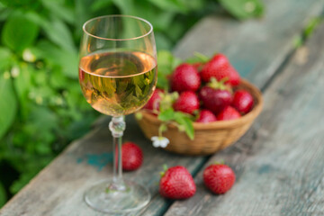 Glass of rose wine served with fresh strawberries on wooden background. Picnic outdoor with pink wine and berries.