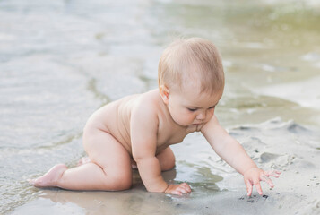 beautiful naked baby plays on the beach in the sand