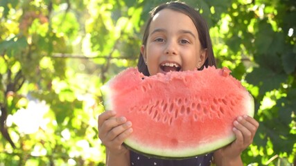 Happy child eating watermelon. Kid eat fruit outdoors. Little girl playing in the garden biting a slice of watermelon.