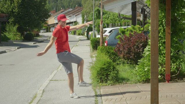 SLOW MOTION: Lazy young delivery guy throws and kicks packages in someone's driveway on sunny day in suburbs. Careless Caucasian courier makes his deliveries around the idyllic suburban neighborhood.