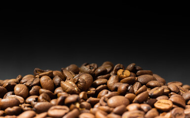 Roasted coffee beans on black background. Heap of coffee beans. Poured coffee close-up