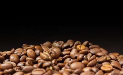 Roasted coffee beans on black background. Heap of coffee beans. Poured coffee close-up