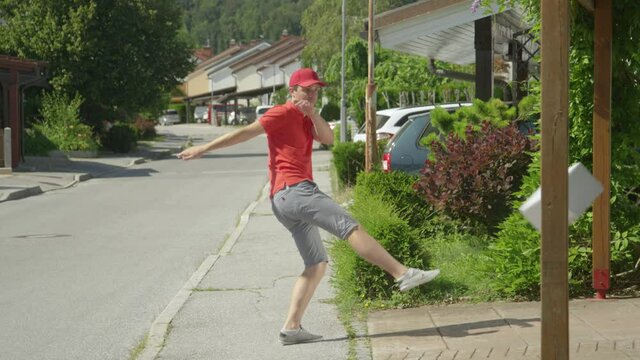SLOW MOTION: Rude millennial courier making his round around the idyllic suburbs kicks three parcels into unknown customer's driveway. Reckless young man carelessly delivering packages on a sunny day.