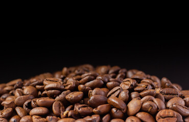 Coffee beans on a black background. Heap of coffee beans. Poured coffee close-up