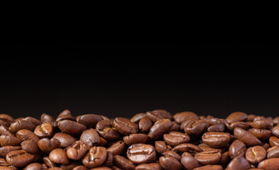 Coffee beans on a black background. Heap of coffee beans. Poured coffee close-up
