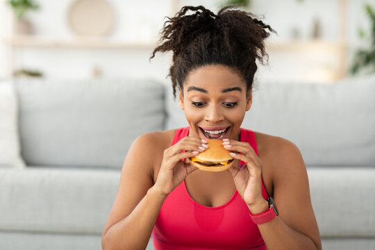 Fit African Woman Biting Burger Eating Fast Food At Home