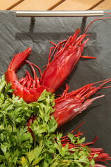 large raw red king prawns on a black background close up with a bunch of fresh parsley