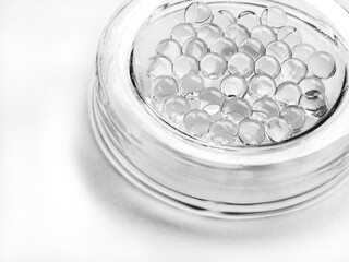 Many tiny transparent, black and white balls in a white glass jar on a white background.