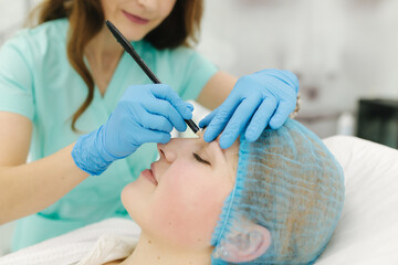 Hands of cosmetologist making preparation for face contouring plasty. Young woman gets beauty facial injections in salon. Aesthetic cosmetology