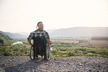 Obraz premium Young man in wheelchair enjoying fresh air in sunny day on the mountains. People with disabilities travelling.