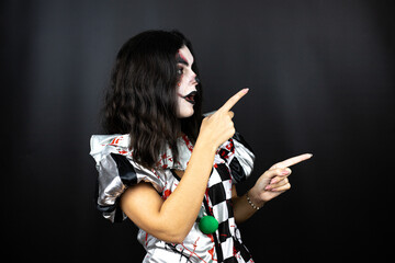 woman in a halloween clown costume over isolated black background surprised, looking side and pointing side with fingers and raised arms