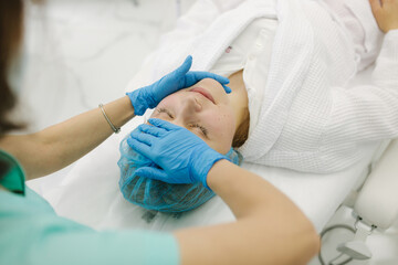 Cosmetoligist make facial massage in beauty salon. Preparing for injection. Cosmetologist in protective medical mask