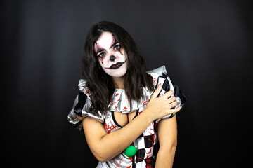 woman in a halloween clown costume over isolated black background with pain on her shoulder and a painful expression