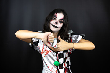 woman in a halloween clown costume over isolated black background Doing thumbs up and down, disagreement and agreement expression. Crazy conflict