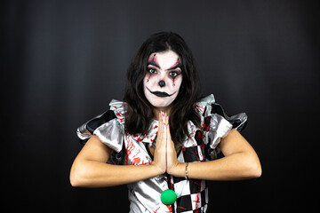 woman in a halloween clown costume over isolated black background begging and praying with hands together with hope expression on face very emotional and worried