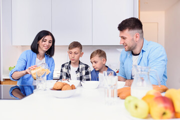 Happy family with two sons eating healthy morning breakfast with cornflakes and milk on cozy kitchen at dining table.
