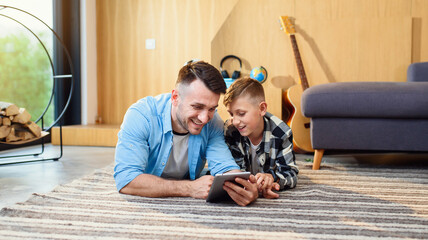 Young boy with father lying on the floor using tablet pc in modern apartment. Happy family time together.