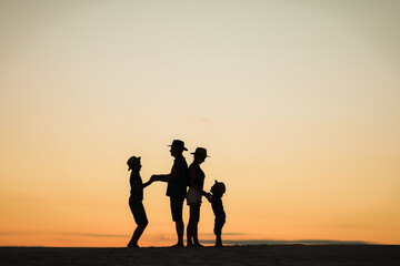Silhouette of a family at sunset on the Sands. Mom and dad stand with their backs to each other and hold hands with their sons.