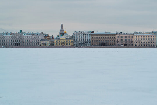Winter embankment of Saint Petersburg with colorful neat buildings stands on banks of frozen Neva river in snow. European city, cloudy light day