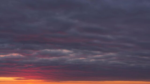 Time lapse of moving dense clouds, illuminated from beneath by setting down sun. burned purple, orange and dark grey sky. Fireworks at the end of the footage. 4K
