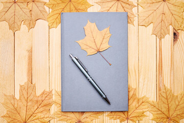 blank diary or book on a wooden desk. decorated with fall maple leaves. minimal composition. above view. planning or story telling concept