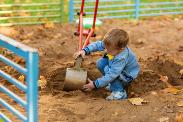 Little boy plays with a toy excavator on the playground in the autumn park.