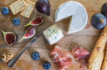 Wooden board with cheese, figs, bread, ham, blueberries and nuts. Top view.