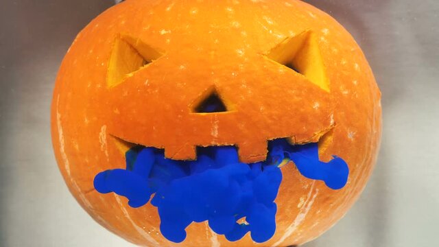 Special paint of blue colour appears from fearful Halloween pumpkin cut mouth and nose against blurred water extreme closeup