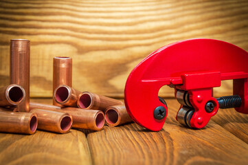 Copper pipes and red pipe cutter with connectors for plumbing repairs on vintage wooden boards...