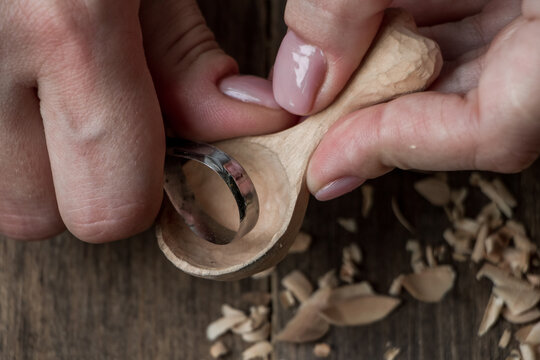 Handmade wooden utensils, top view female hands carve a wooden spoon with stock-knife, selective focus