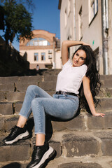 Sexy woman in denim sits on stairs in the city. woman with beautiful smile