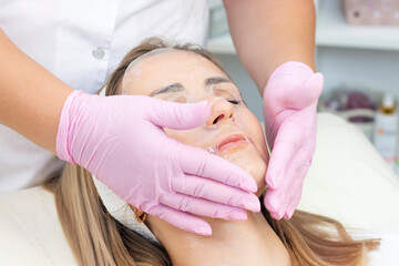 cosmetology. Close up picture of lovely young woman with closed eyes receiving facial cleansing procedure in beauty salon.