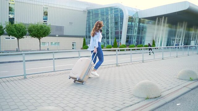 Young Stylish Girl Hipster Tourist Runs a Suitcase is Late for Departure to the Airport or Bus Station Train in the City Urban Background. Woman Traveling Student Running Hurried down Street