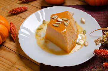 Flan de calabaza. Postre elaborado con calabaza,  servido en plato blanco, sobre mesa de madera decorado con tema otoñal.