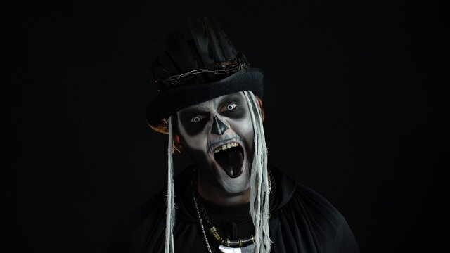 Frightening man in skeleton Halloween cosplay costume. Guy in creepy skull makeup making faces