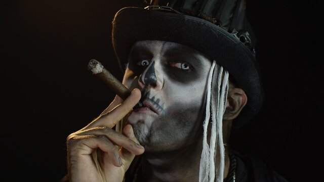 Sinister man with horrible Halloween holiday skeleton makeup raising his head and smoking cigar