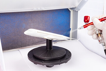 paint job with red metal airbrush spray paint gun on red scale model modern white blue passenger airplane plane in paint booth. hobby industry concept background