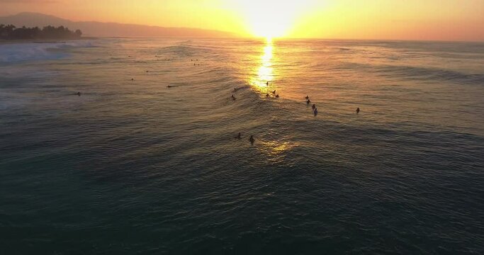 Sunset over group of surfers in Hawaii, wide aerial