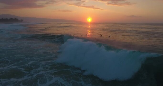 Surfers catch waves at sunset in Hawaii, wide aerial