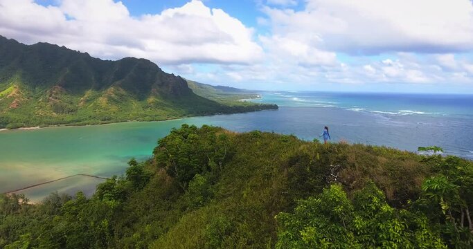 Panning aerial, woman hikes on coastal mountain ridge in Hawaii
