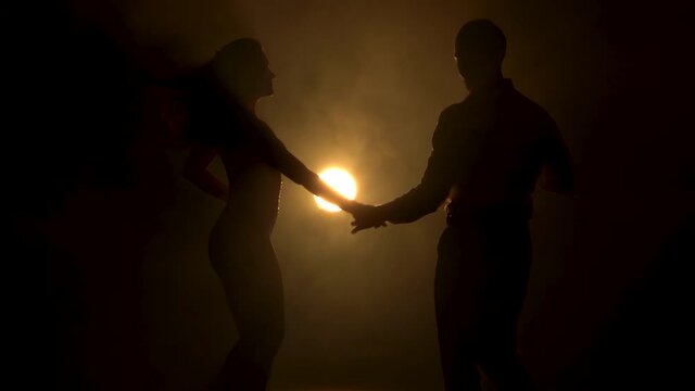 Portrait of two sensual latin dancers dancing a sexy dance in a dark smoky studio with yellow light. Young couple dancing salsa in slow motion. Close up.