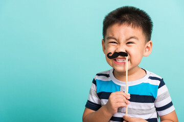 Funny happy hipster kid holding black mustache props for the photo booth close face, studio shot...