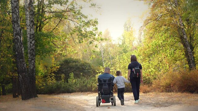 wheelchair man. Handicapped man. young disabled man in an automated wheelchair walks with his family, wife and small child, in the park, on sunny autumn day. back view