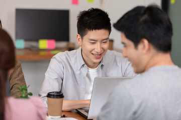 Fototapeta premium Happy Asian business young man smile and working with laptop and their team in co-working space or modern office,Business Teamwork Collaboration Concept